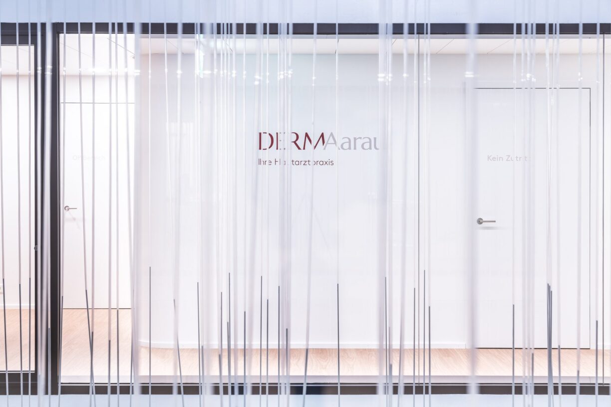 Lichthof mit Glaswand und Praxislogo DERMAarau