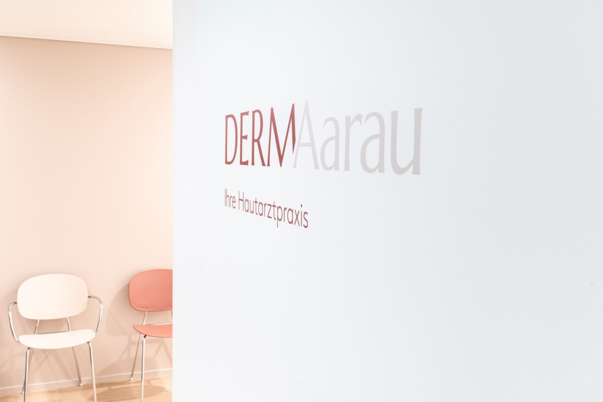 Wartebereich mit Stühlen vor der Wand mit dem Praxislogo «DERMAarau – Ihre Hautarztpraxis»